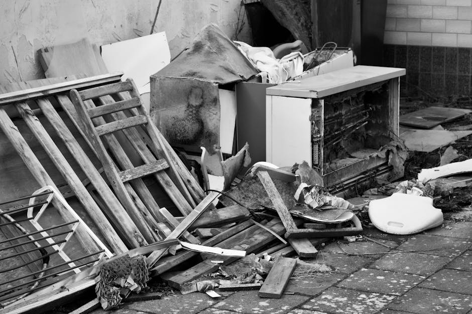 A large pile of discarded furniture and household items, including various wooden desks, chairs, and tables, along with some office equipment and packaging materials such as cardboard and plastic wrap